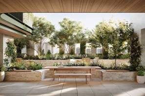 Un patio al aire libre con un banco de madera, macetas de piedra y vistas a un edificio con ventanas con rejas.