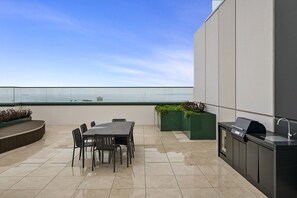 Eine Dachterrasse mit Esstisch, Stühlen, einem Grill und Pflanzenkübeln.