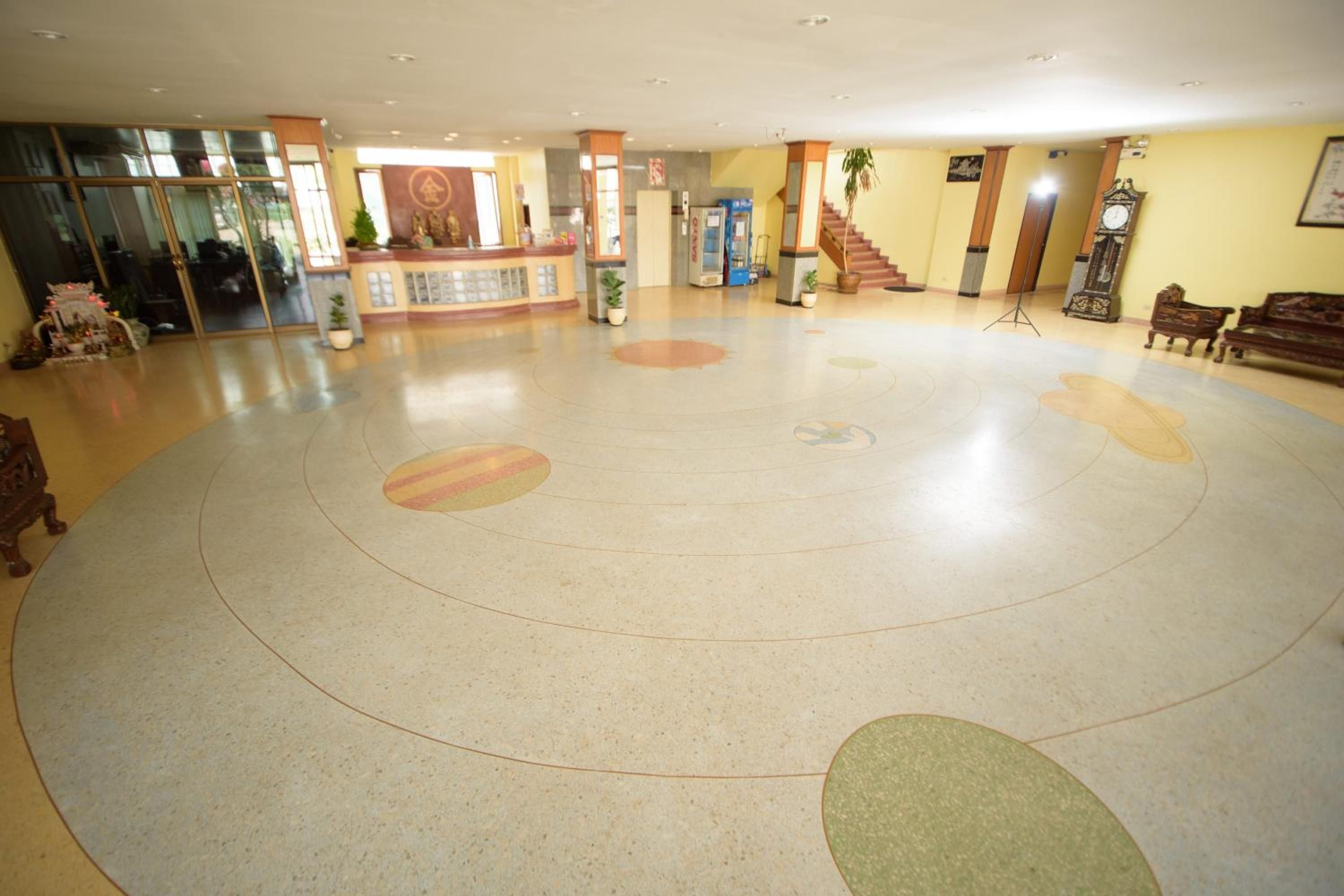 A spacious lobby with a reception desk, a staircase, and a large circular patterned floor.