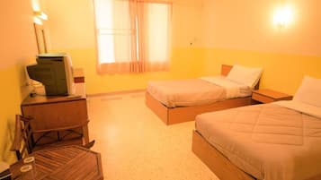A room with two beds, a desk with a computer, a chair, and a window with curtains.