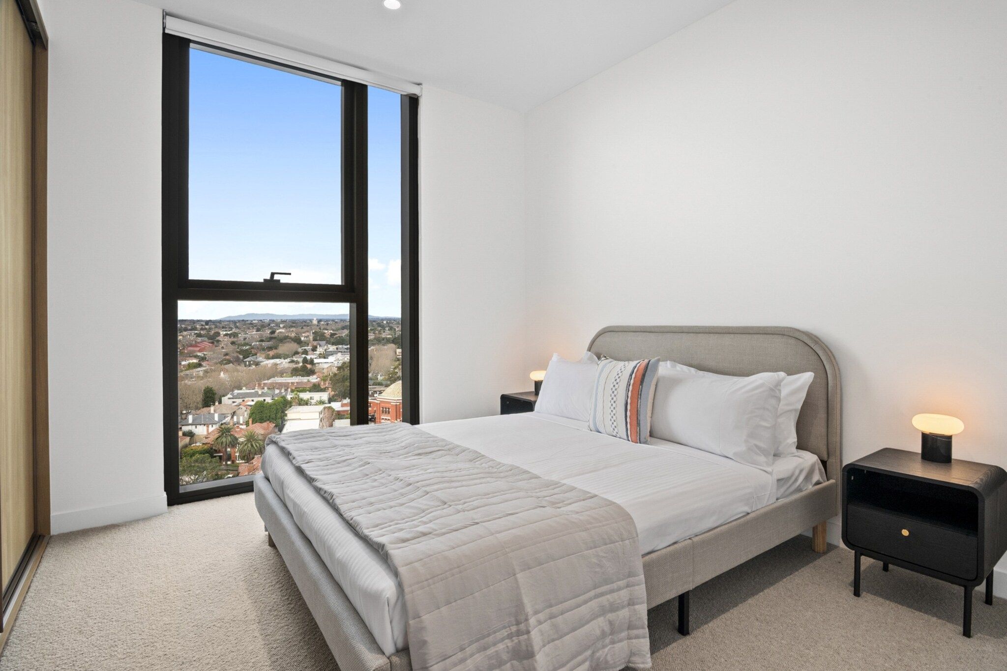 A bedroom with a large bed, two bedside tables, and a view of a cityscape through a large window.