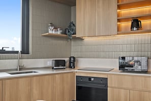 A modern kitchen with a dishwasher, a coffee maker, and a toaster. - Balcony 3-Bed Apartment Near Albert Park (St Kilda)