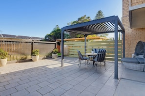 Ein überdachter Patio-Bereich mit Tisch, Stühlen, Topfpflanzen und einer Ziegelwand.