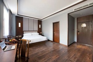 Une chambre d’hôtel avec un lit, un bureau avec un ordinateur portable, une chaise et un plancher en bois.
