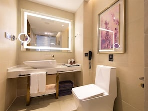 Un baño moderno con un espejo grande, un lavabo, un inodoro y una obra de arte enmarcada en la pared.