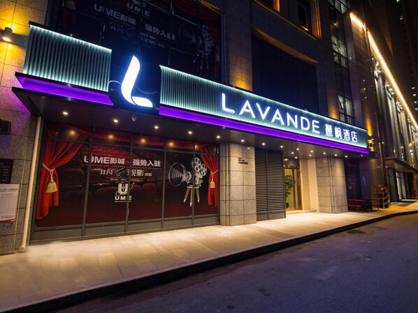 A hotel entrance with a prominent sign, a tiled facade, and a sidewalk in front.