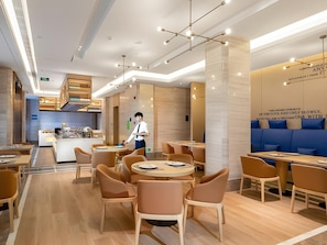Interior moderno de restaurante con mesas redondas, sillas acolchadas, una zona de bar y un área de estar con cojines azules.