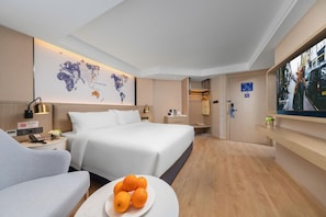 Habitación de hotel con una cama grande, un escritorio, una silla, un mapa del mundo en la pared y un televisor.
