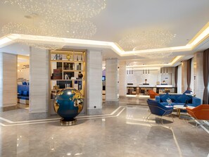 Un vestíbulo de hotel moderno con un globo terráqueo como pieza central, una zona de estar con sofás azules y un bar.