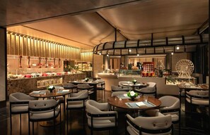 Un restaurant avec des tables et des chaises rondes, un coin bar et un présentoir à desserts.