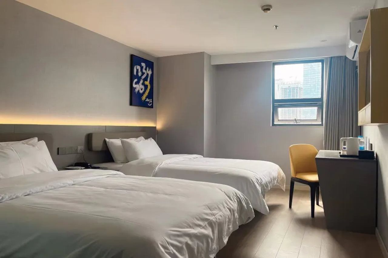 A hotel room with two beds, a desk, a chair, a window, and a wall-mounted artwork.