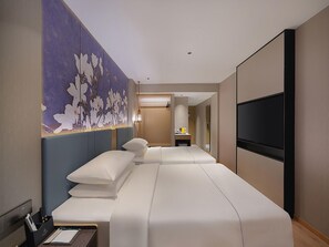 Camera d'albergo con un letto grande, una TV, una scrivania con una lampada e un murale floreale sulla parete.