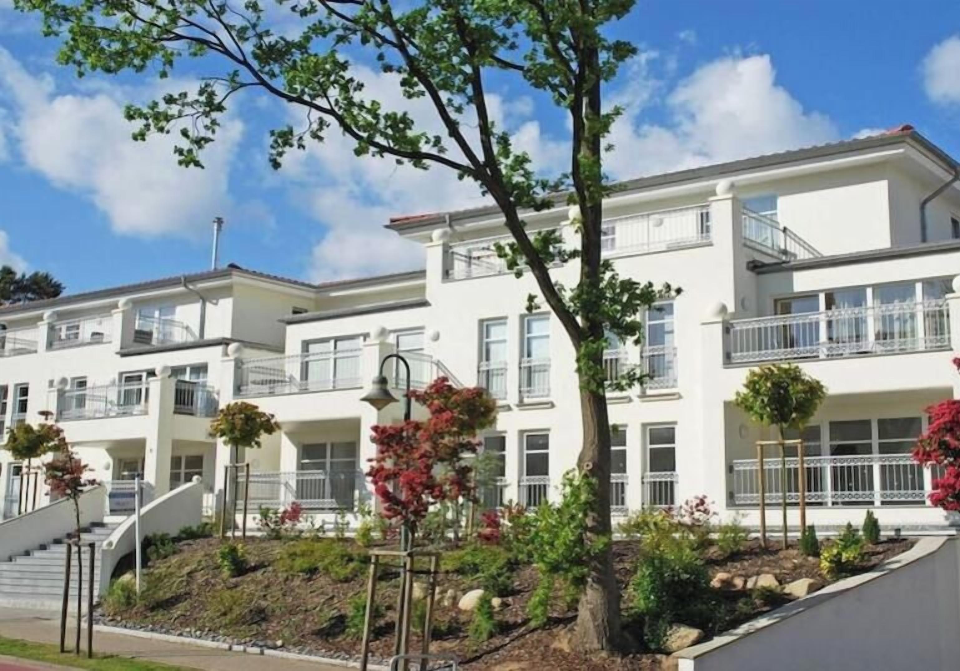 A multi-story residential building with balconies, a landscaped garden, and a clear sky.