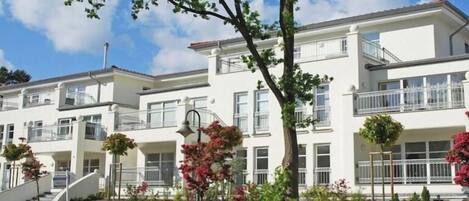 A multi-story residential building with balconies, a landscaped garden, and a clear sky.
