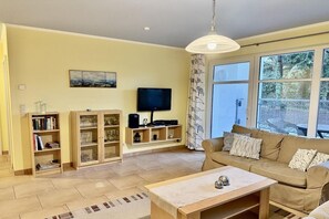 A living room with a sofa, a coffee table, a TV, and a bookshelf. - Queen Augusta Dune Residence 2 (Ostseebad Binz)