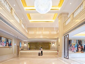 Um saguão de hotel com uma recepção, um lustre grande e um quadro na parede.