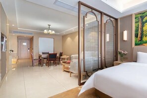 Quarto de hotel com cama, escrivaninha, cadeira, mesinha e zona de chuveiro.