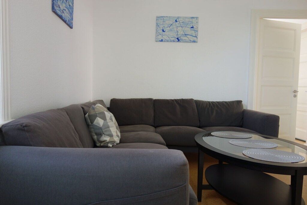 Een moderne woonkamer met een hoekbank, een glazen salontafel en abstracte wanddecoratie.