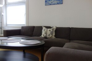 Ein Wohnzimmer mit einer Eckcouch, einem runden Couchtisch und einem Fenster mit Jalousien.