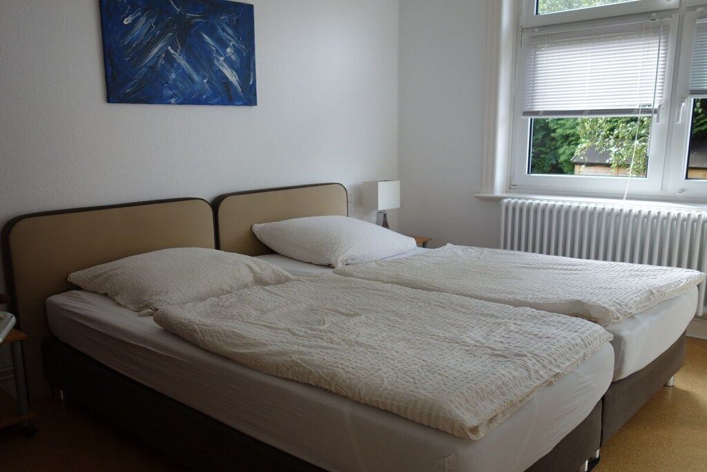 Une chambre avec deux lits, un radiateur, une fenêtre avec des stores et un tableau accroché au mur.