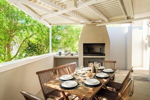 An outdoor dining area with a table set for six, surrounded by wooden chairs, and a built-in grill in the background. - Green Point 4 Bed Family Home w Pool Happy House (Cape Town)