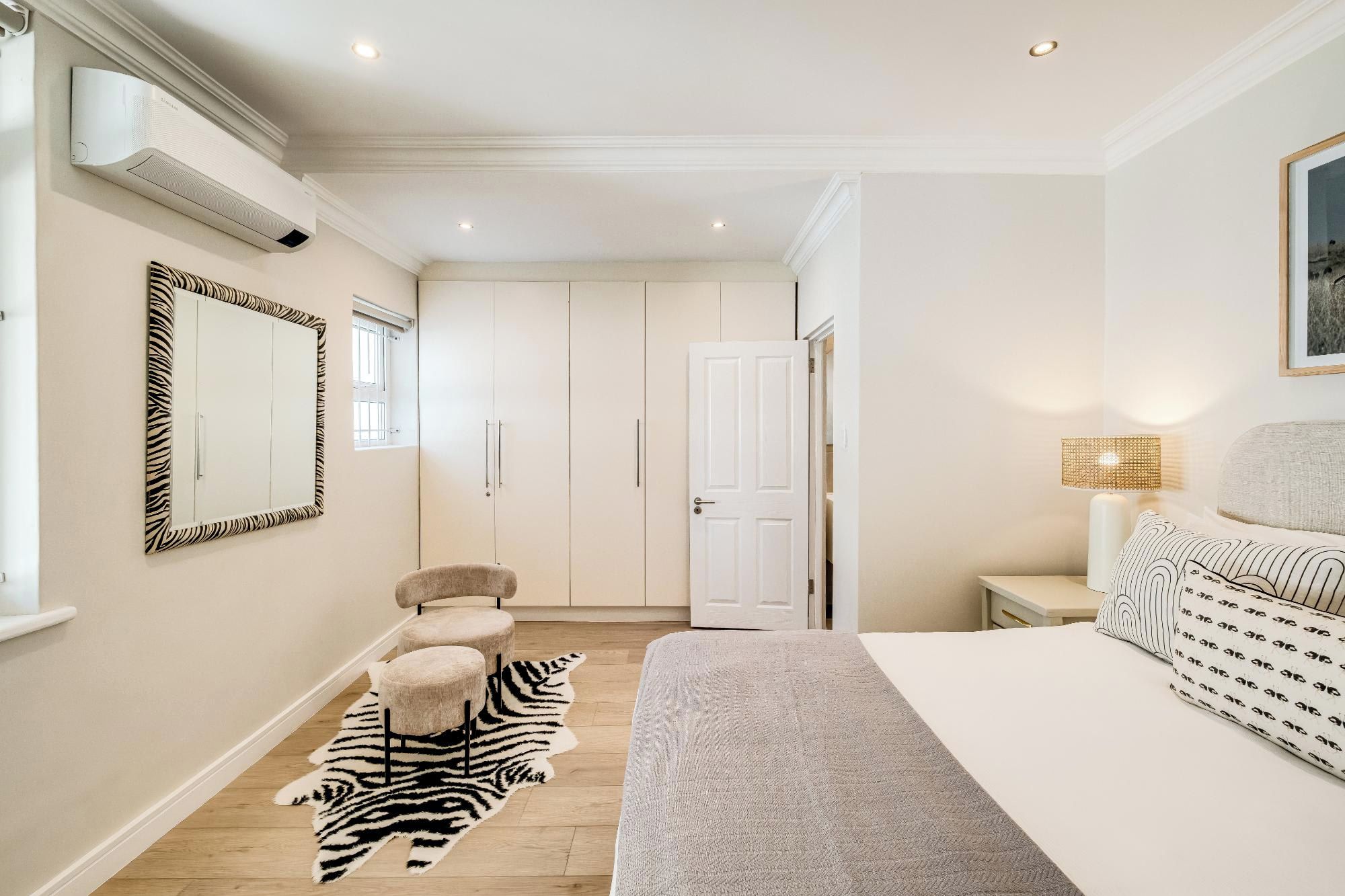 A bedroom with a bed, a zebra-patterned rug, a white wardrobe, and a zebra-patterned mirror.