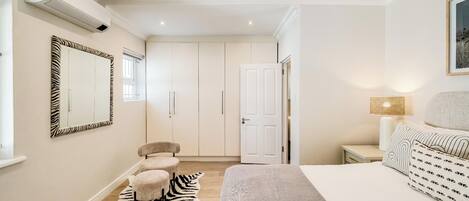 A bedroom with a bed, a zebra-patterned rug, a white wardrobe, and a zebra-patterned mirror.