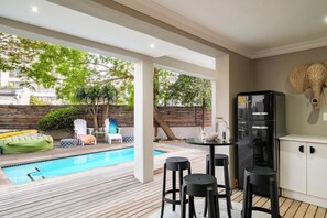 A modern outdoor living area with a pool, bar stools, and a refrigerator. - Green Point 4 Bed Family Home w Pool Happy House (Cape Town)