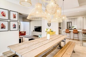 A modern kitchen with a dining area, featuring a wooden table and bench, a TV, and a yellow cabinet. - Green Point 4 Bed Family Home w Pool Happy House (Cape Town)