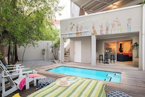 A pool area with a wooden deck, lounge chairs, and a dining area with stools. - Green Point 4 Bed Family Home w Pool Happy House (Cape Town)