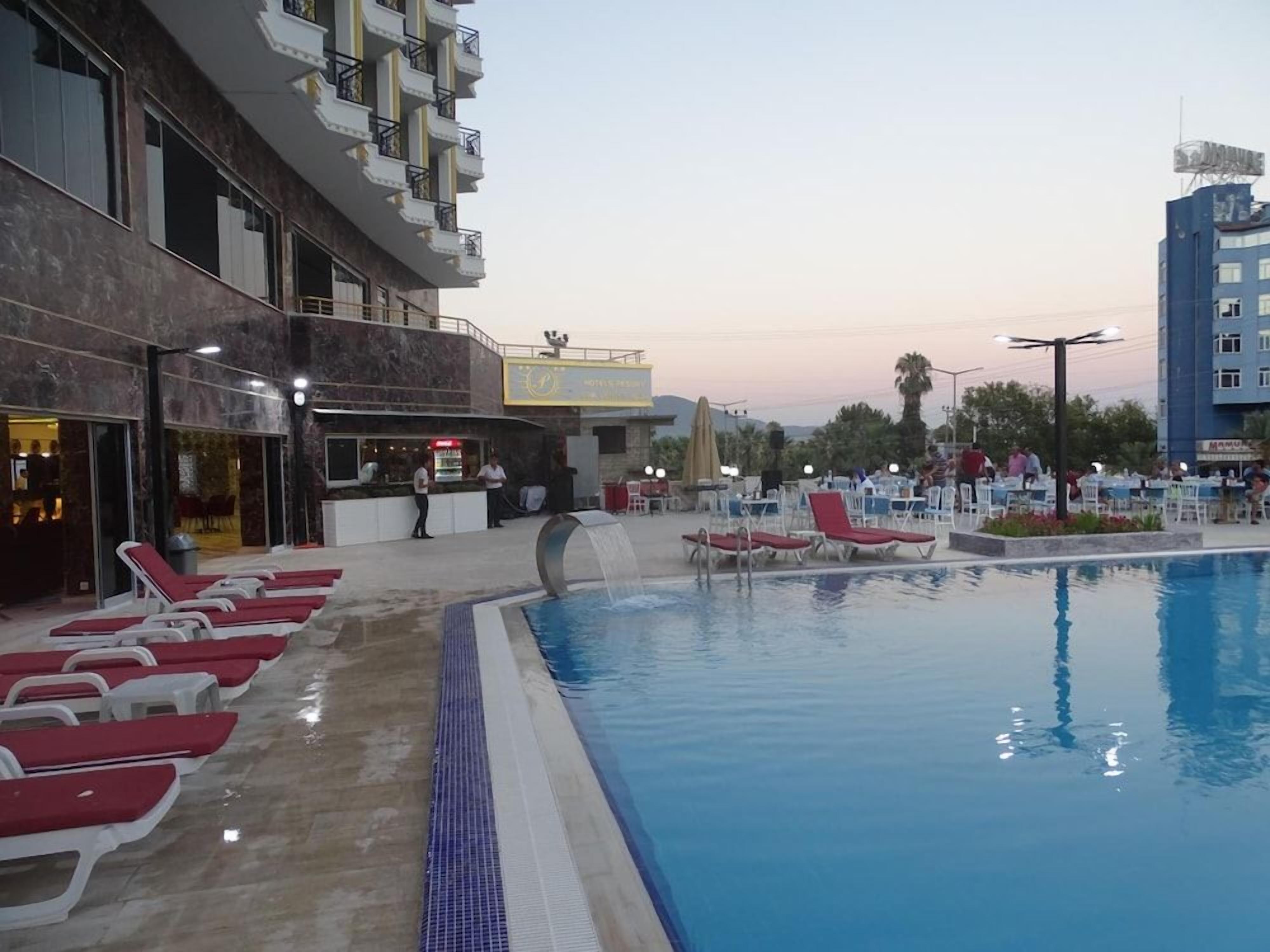 A swimming pool with sun loungers, a bar area, and a hotel building with balconies.