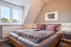 A bedroom with a sloped ceiling, a large bed with a headboard, a window with curtains, and a framed picture on the wall. - TOPP in the Captain's House Ostseerose (Travemünde)