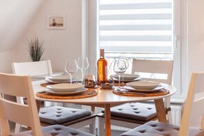 A dining table set for four with plates, glasses, and a bottle, surrounded by cushioned chairs. - TOPP in the Captain's House Ostseerose (Travemünde)