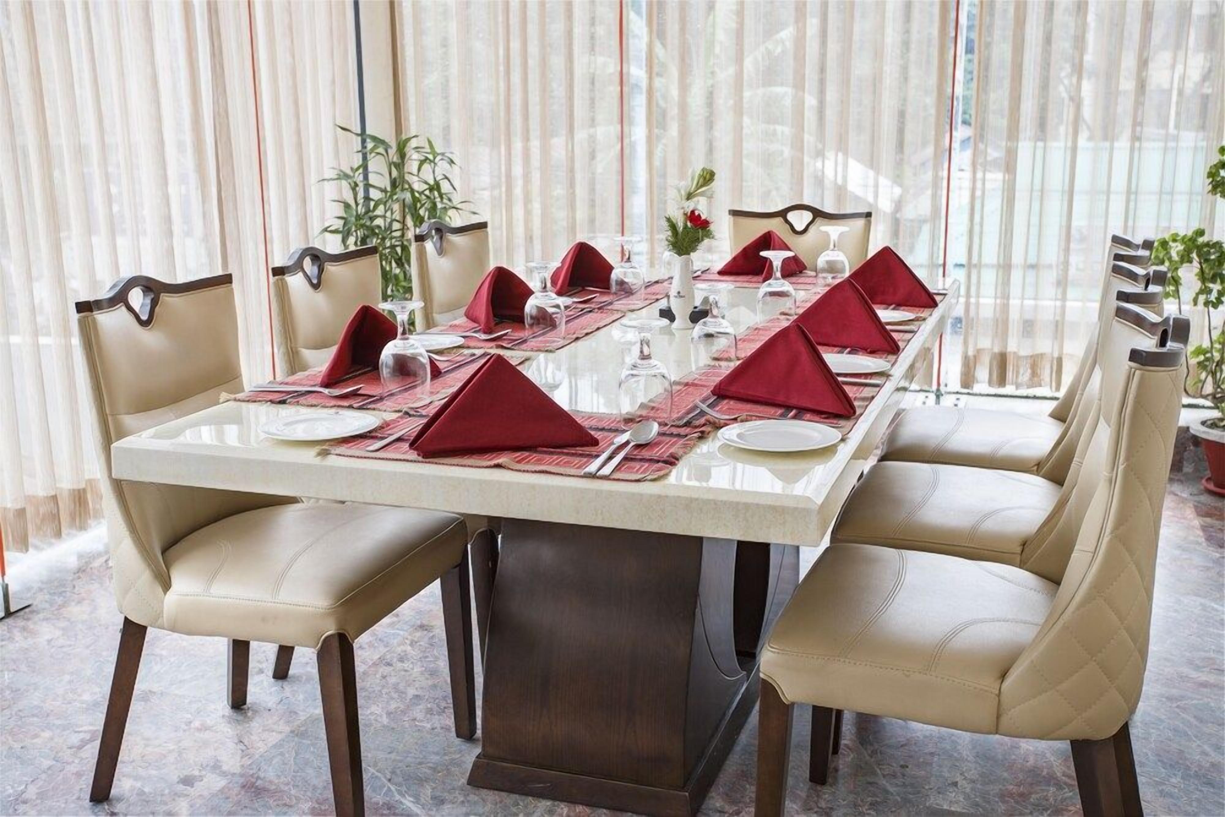 A dining table set for six with red napkins, white plates, and clear glassware.