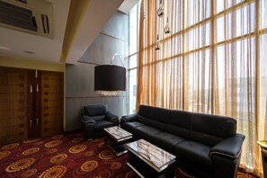 A modern hotel room with a black leather sofa, a matching armchair, and a patterned carpet.