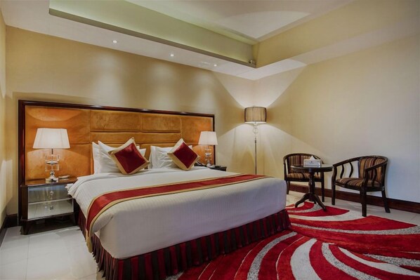 A hotel room with a large bed, two bedside lamps, a red and white striped rug, and a small table with chairs.