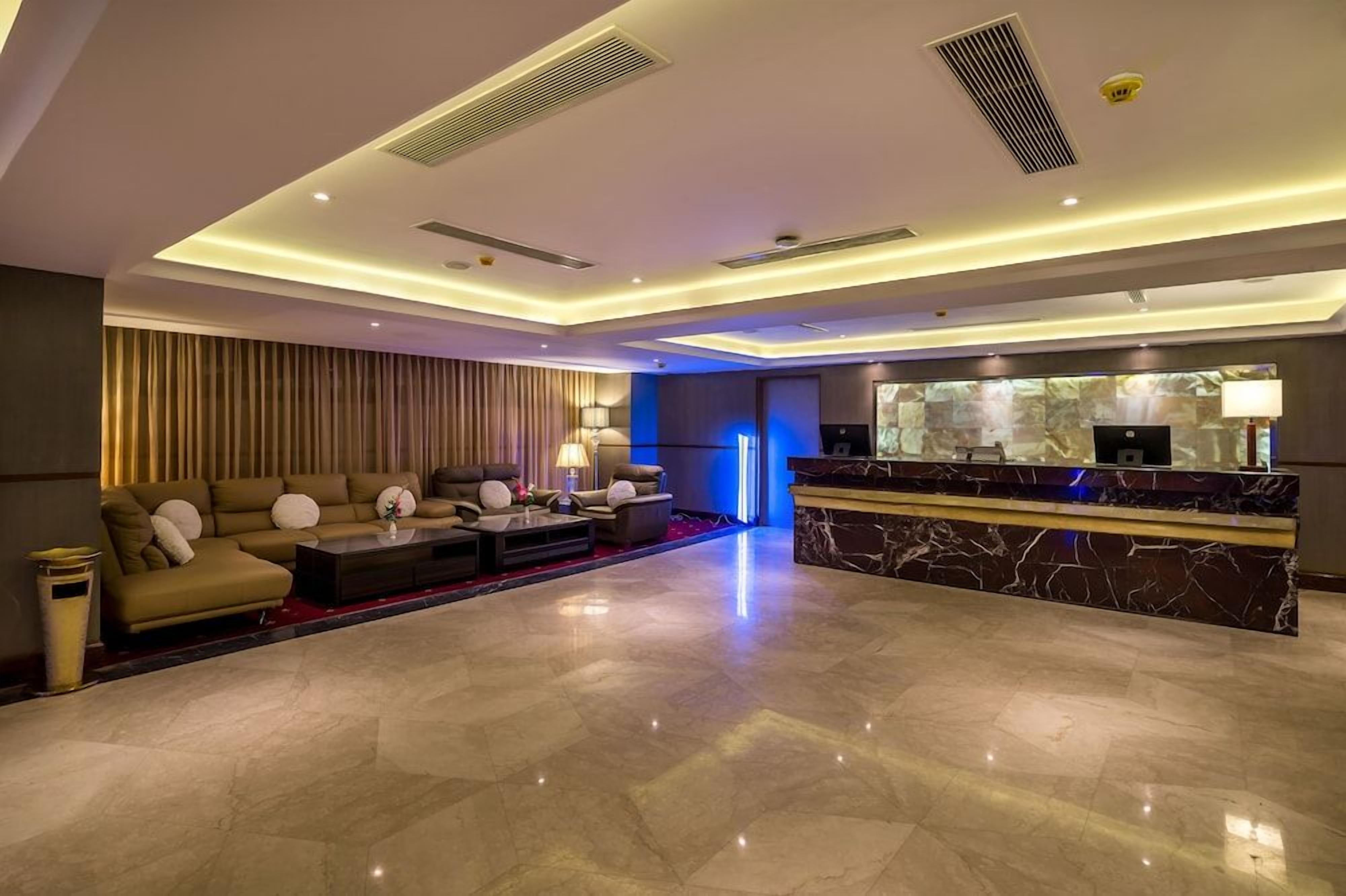 A modern hotel lobby with a reception desk, seating area, and a large mirror.