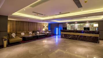 A modern hotel lobby with a reception desk, seating area, and a large mirror.