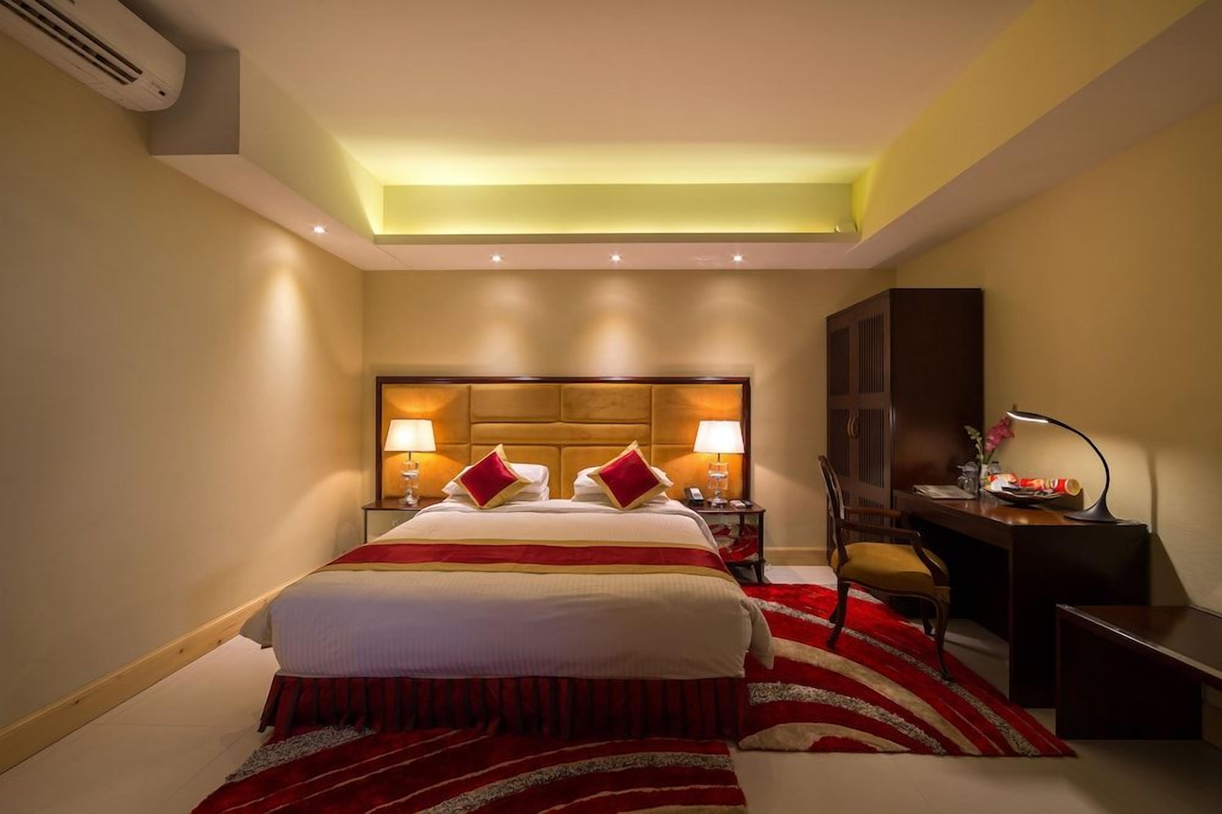 A hotel room with a large bed, two bedside lamps, a desk with a chair, and a television.