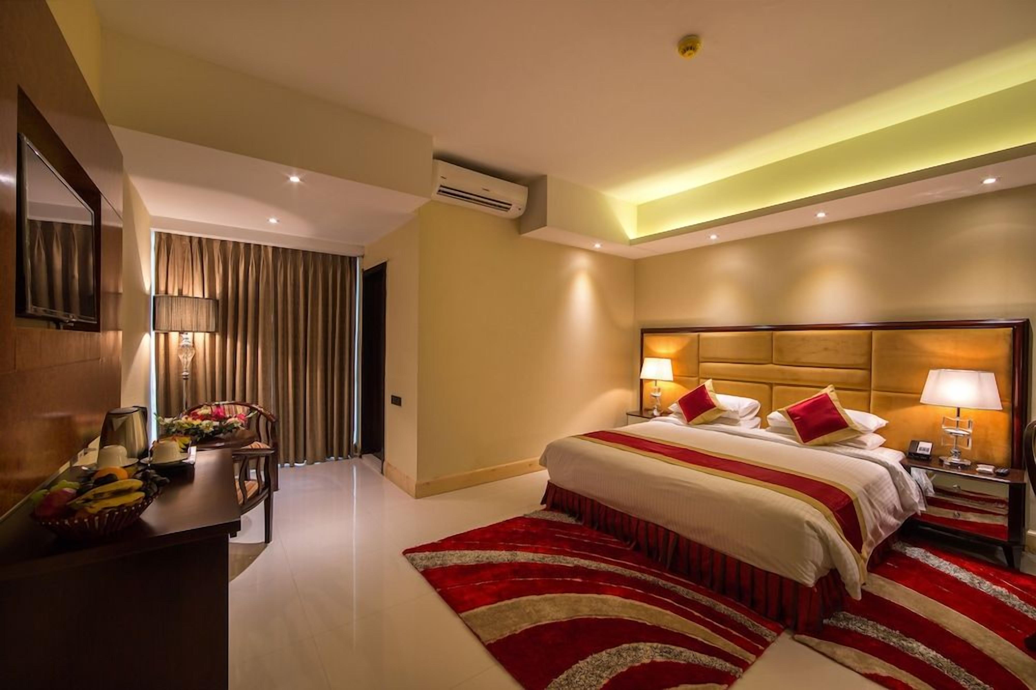 A hotel room with a large bed, bedside lamps, a desk with a telephone, and a red and white striped area rug.