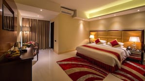 A hotel room with a large bed, bedside lamps, a desk with a telephone, and a red and white striped area rug. - Grand Palace Rangpur (Rangpur)