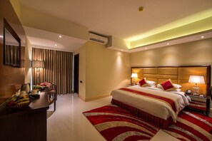 Habitación de hotel con una cama grande, lámparas de noche, un escritorio con teléfono y un tapete a rayas rojo y blanco.