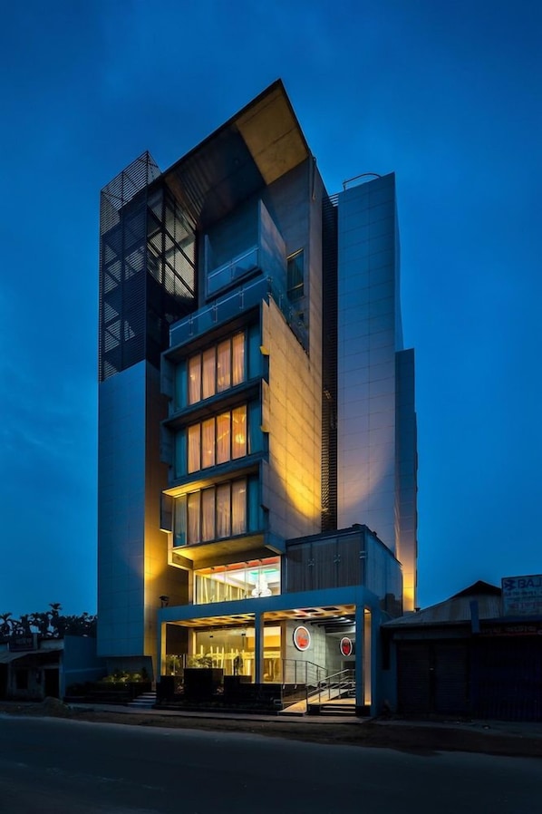 Un edificio de varios pisos con un diseño arquitectónico moderno, que destaca una entrada principal con puertas de cristal y un letrero visible de un restaurante.