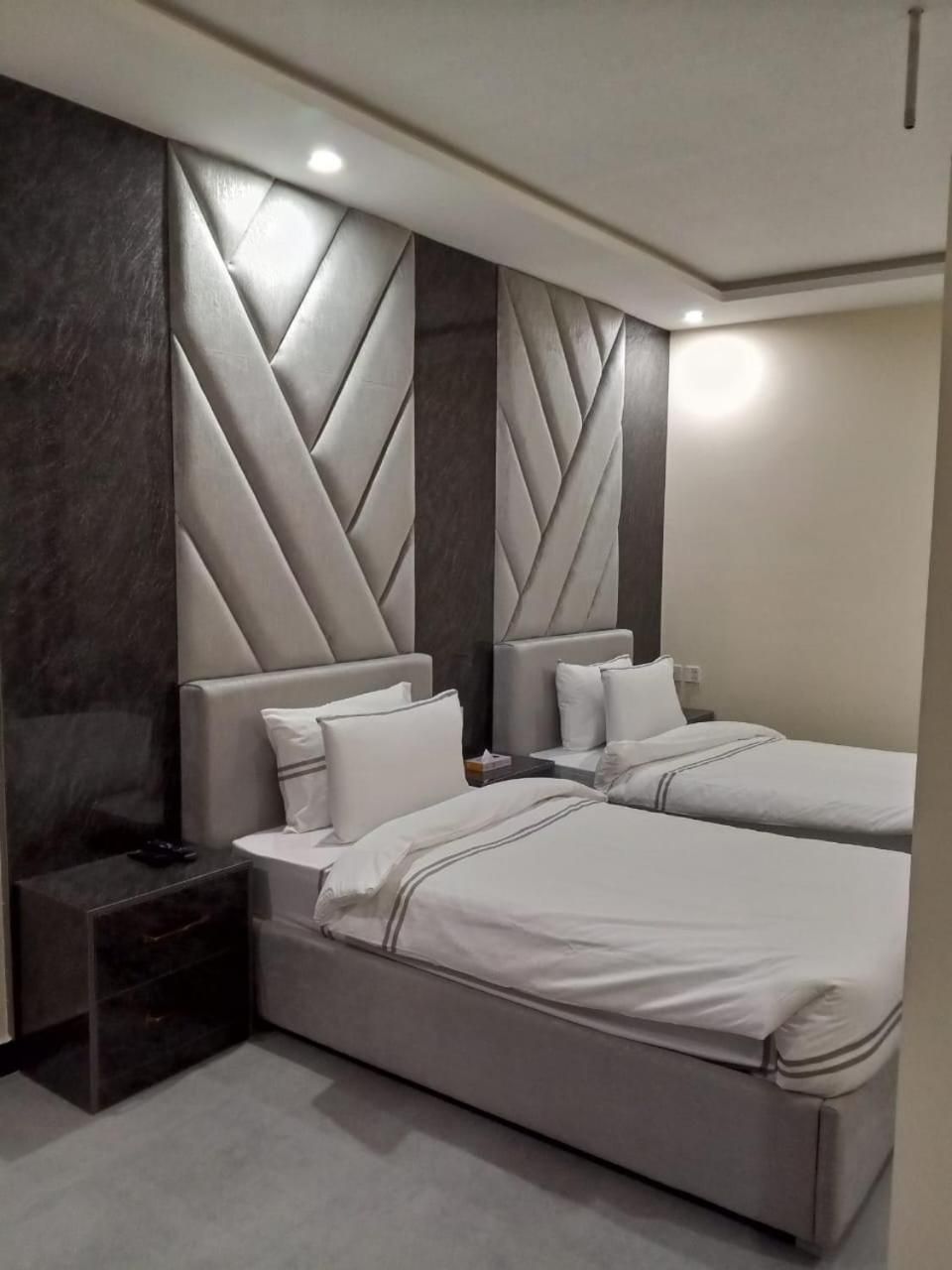 A hotel room with two beds, a dark accent wall, and a modern headboard design.