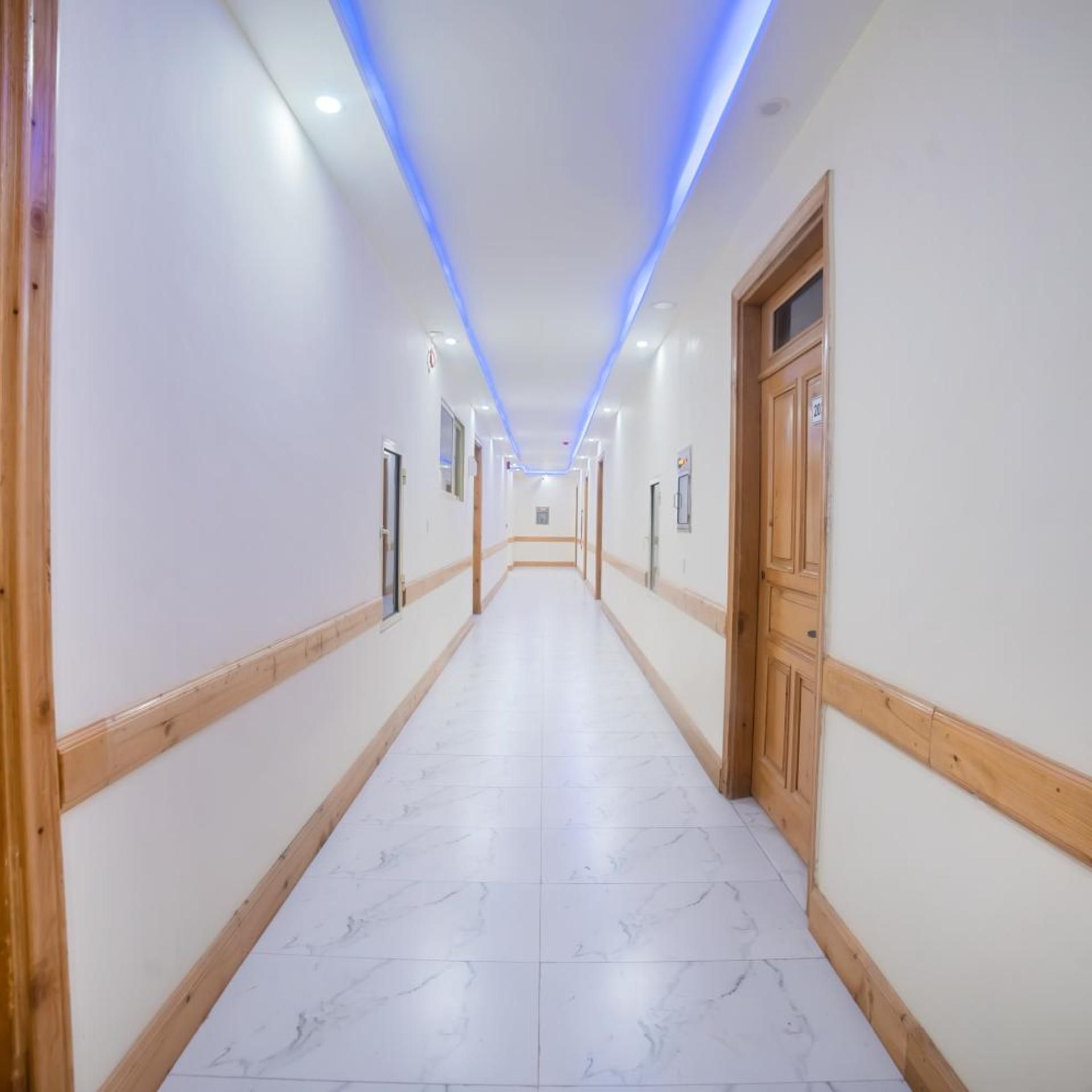 A long, narrow hallway with white walls and wooden trim, leading to a door at the end.