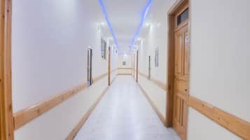 A long, narrow hallway with white walls and wooden trim, leading to a door at the end.