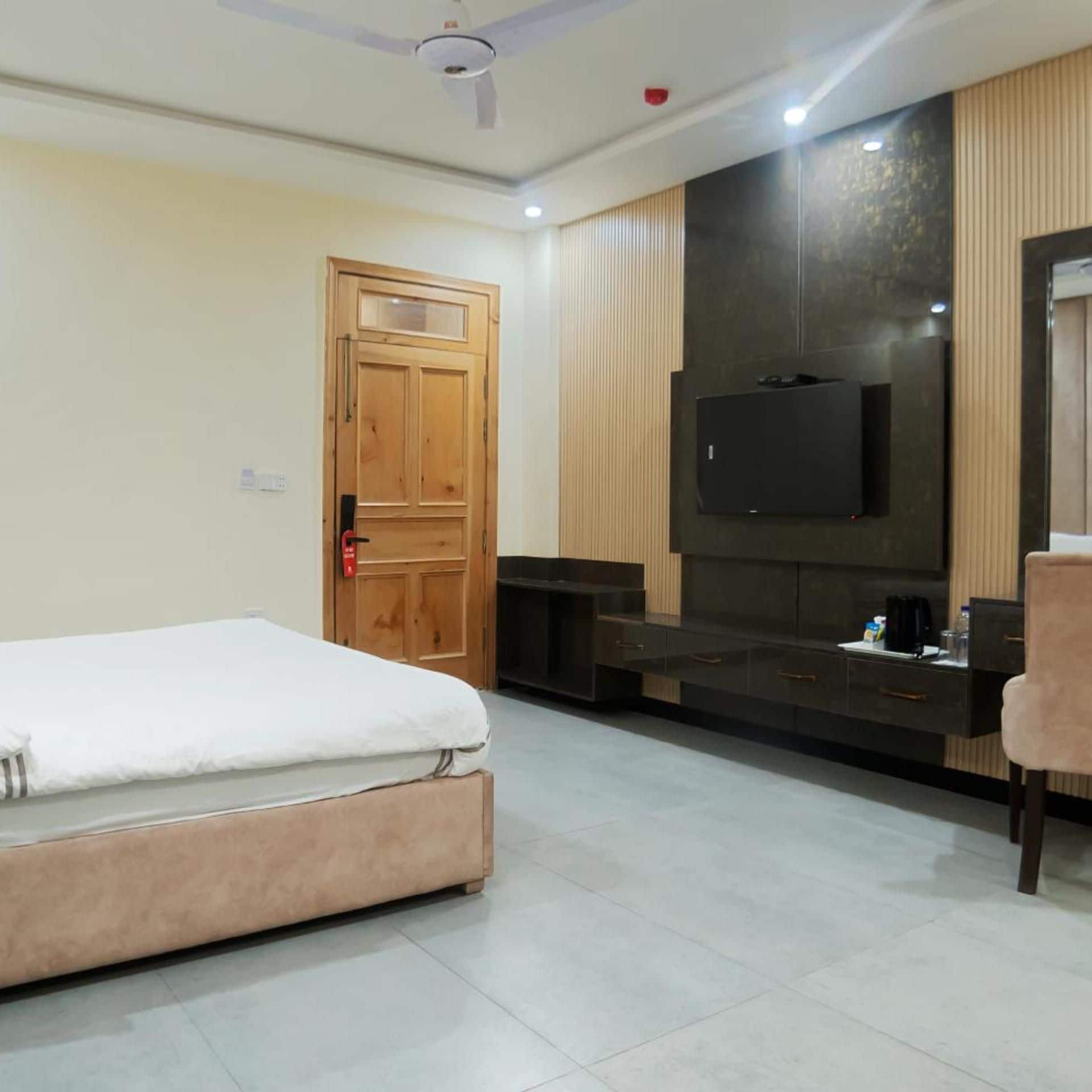 A hotel room with a bed, a TV mounted on the wall, a seating area with a sofa, and a wooden door.