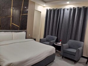 Una habitación de hotel con una cama grande, dos sillones, una mesita redonda y una cortina.