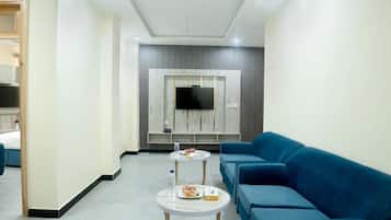A modern hotel room with a blue sofa, a round coffee table, and a flat-screen TV mounted on the wall.