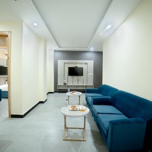 A modern hotel room with a blue sofa, a round coffee table, and a flat-screen TV mounted on the wall. - Legend Hotel Kalam (Swat)
